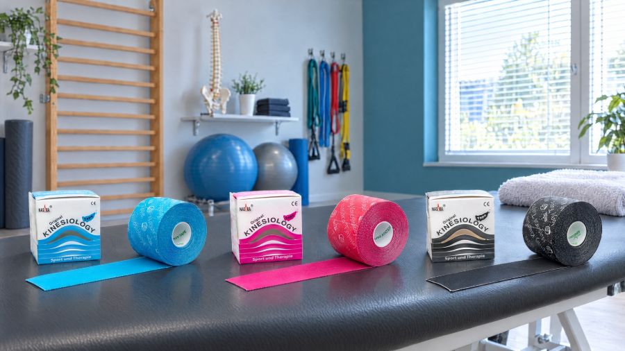 Nasara Kinesio Tape in Blau, Pink und Schwarz mit den Originalverpackungen auf einer Behandlungsliege in einer Physiopraxis.